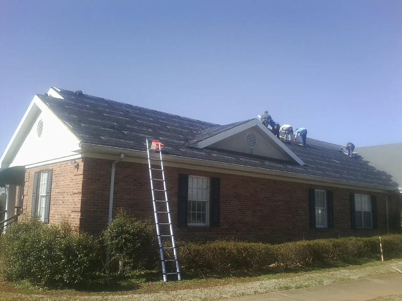 Crew tearing shingles off a brick ranch roof with a ladder set — Emergency Roof Repair work by our crew in Woodberry Forest