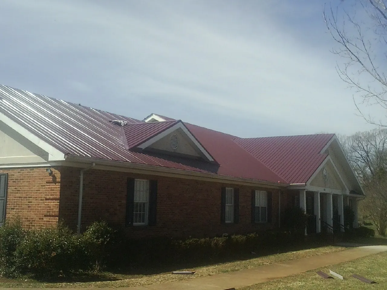 Red metal roof with gabled entries on a long brick building, from a Hail Damage Roof Repair job in Woodberry Forest