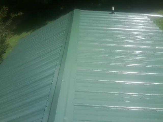 New green metal panels meeting at the ridge of a roof — Flat Roof Repair work by our crew in Woodberry Forest