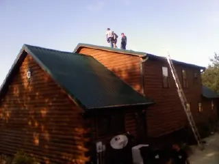 Crew on the ridge of a green metal roof on a two story log home in Woodberry Forest