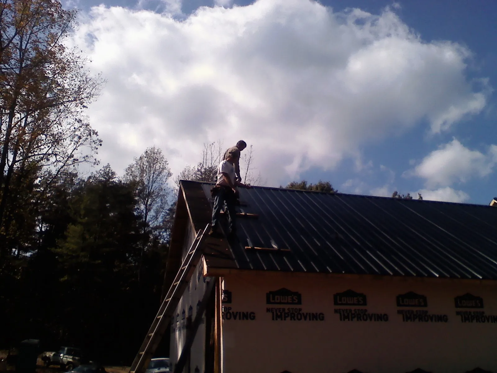 Roofer fastening dark metal panels high against a cloudy sky, from a Roof Inspection job in Woodberry Forest