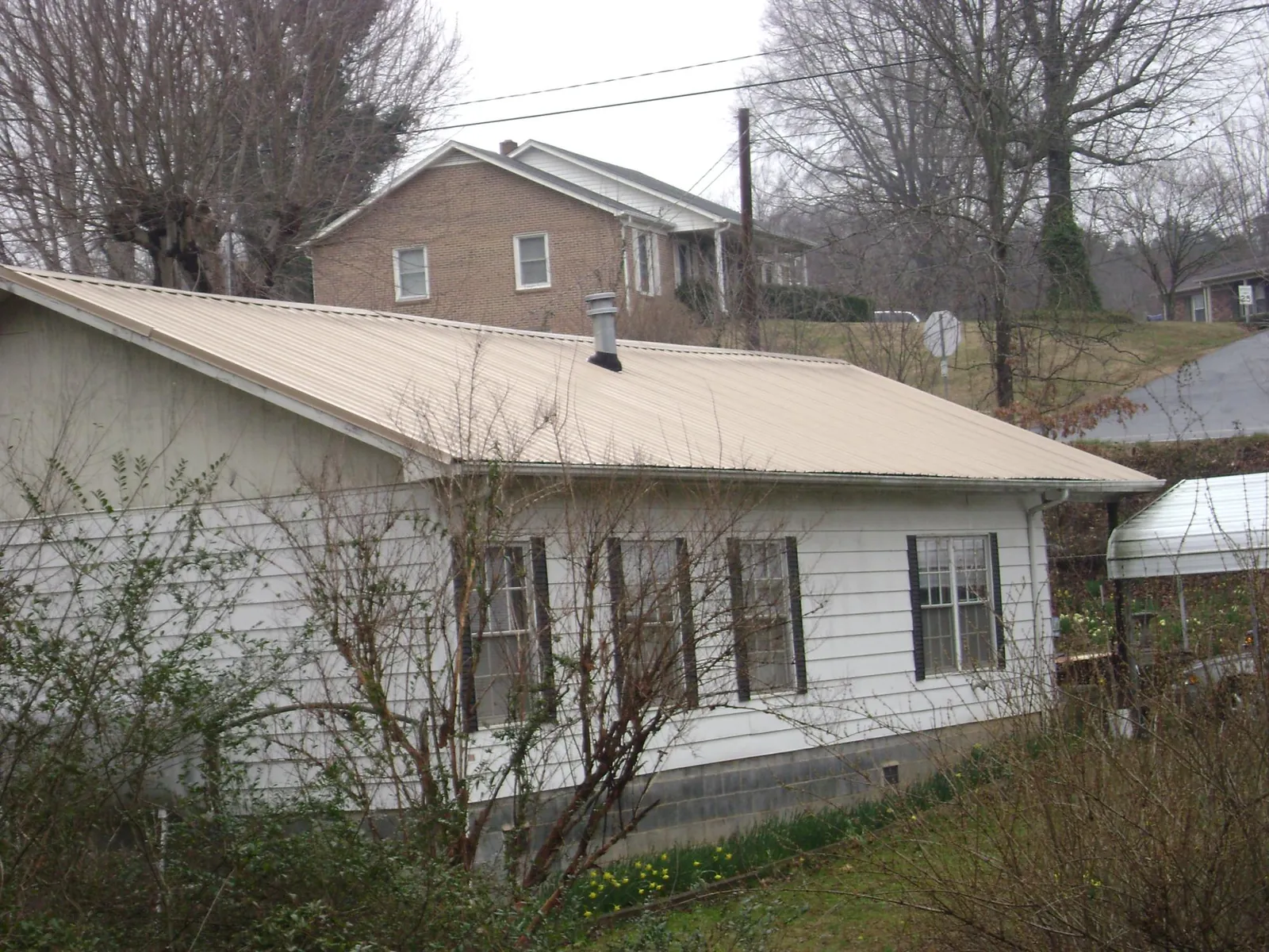 Tan metal roof on a white sided house set into a hillside — Commercial Roofing by Roofing Brothers in Woodberry Forest