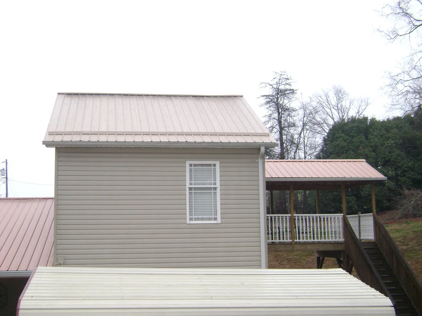 Tan metal roofs on a two story addition and attached porch, from a Roof Replacement job in Woodberry Forest